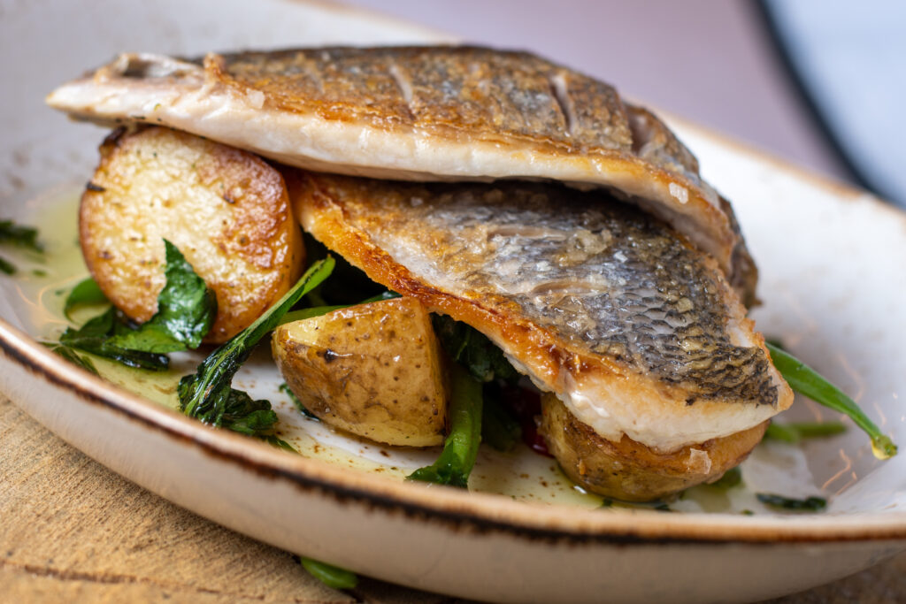 A photo of grilled sea bass on a bed of potatoes and vegetables